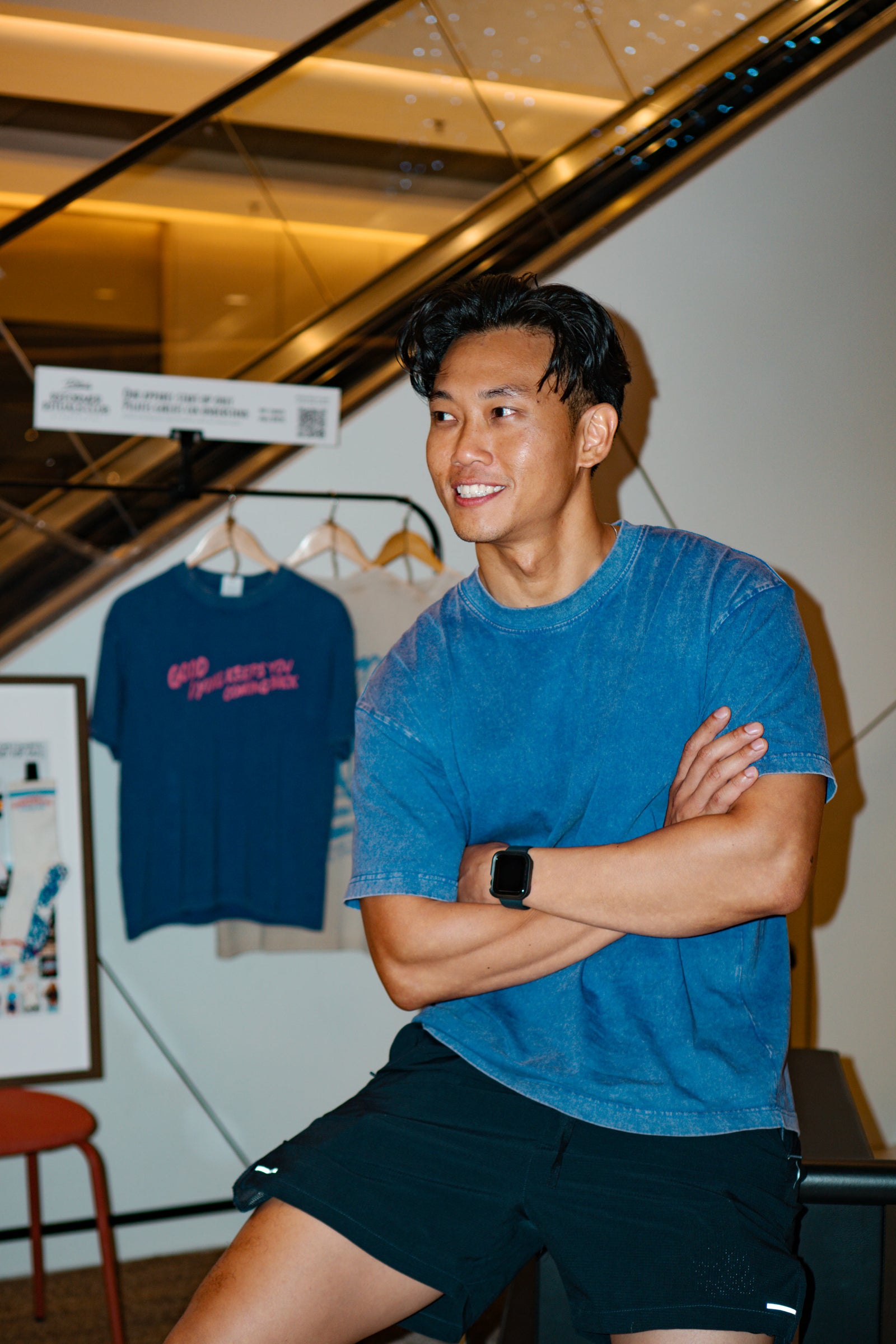 Man in blue shirt and black shorts sitting with arms crossed in a casual setting.